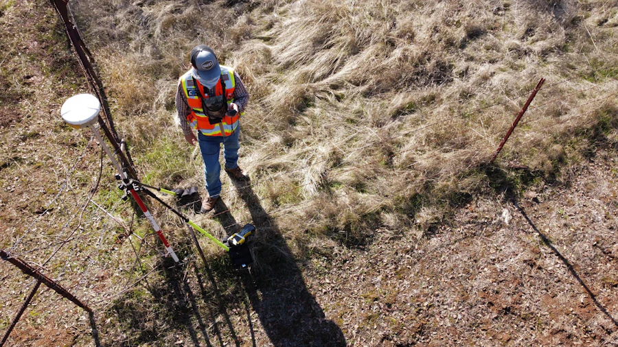 Topógrafo com equipamento GPS/GNSS em levantamento de campo, vista aérea